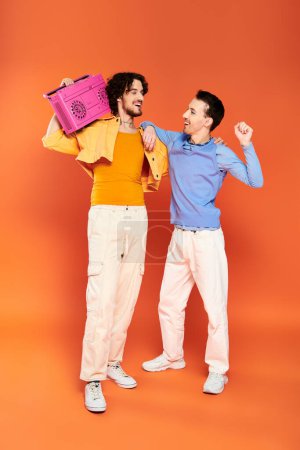 zwei positive attraktive homosexuelle Männer in lebendiger, gemütlicher Kleidung posieren mit Tonbandgerät, stolzer Monat