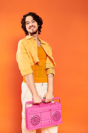 Foto de Sofisticado alegre gay hombre posando alegremente con cinta grabadora en naranja telón de fondo, orgullo mes - Imagen libre de derechos