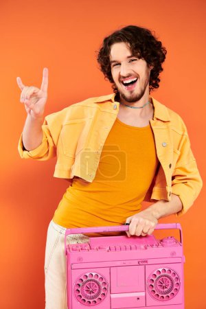 Photo for Fashionable joyous gay man posing cheerfully with tape recorder on orange backdrop, pride month - Royalty Free Image