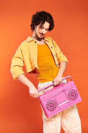 Photo for Good looking joyous gay man posing cheerfully with tape recorder on orange backdrop, pride month - Royalty Free Image