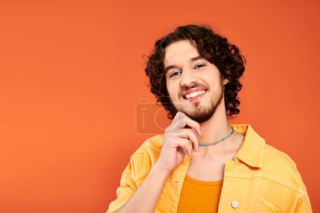 Foto de Alegre atractivo gay hombre con oscuro cabello y vibrante maquillaje posando en naranja telón de fondo, orgullo mes - Imagen libre de derechos
