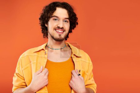 Foto de Alegre atractivo gay hombre con oscuro cabello y vibrante maquillaje posando en naranja telón de fondo, orgullo mes - Imagen libre de derechos