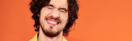 Photo for Attractive jolly gay man with dark hair and makeup posing on orange backdrop, pride month, banner - Royalty Free Image