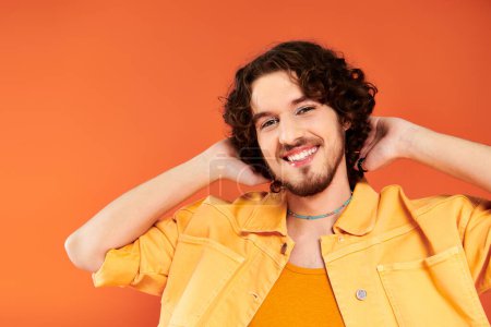 Photo for Joyous appealing gay man with dark hair and vibrant makeup posing on orange backdrop, pride month - Royalty Free Image