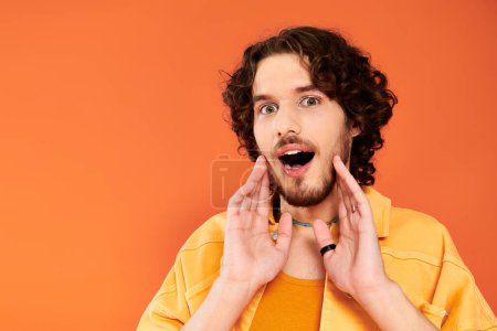 Photo for Cheerful appealing gay man with dark hair and vibrant makeup posing on orange backdrop, pride month - Royalty Free Image