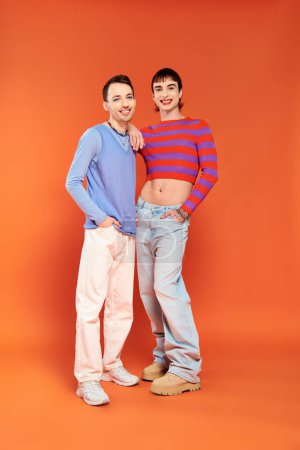Téléchargez les photos : Deux jeunes hommes gays joyeux avec un maquillage vibrant dans des vêtements élégants posant et souriant à la caméra - en image libre de droit