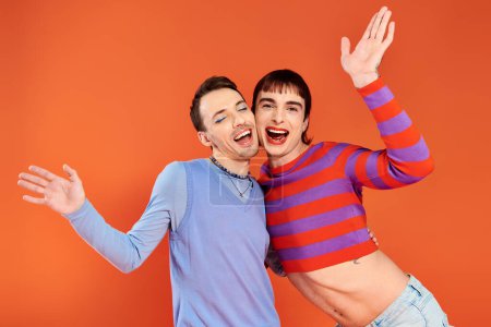 Foto de Alegre atractivo gay amigos con vívido maquillaje posando juntos en naranja telón de fondo, orgullo mes - Imagen libre de derechos