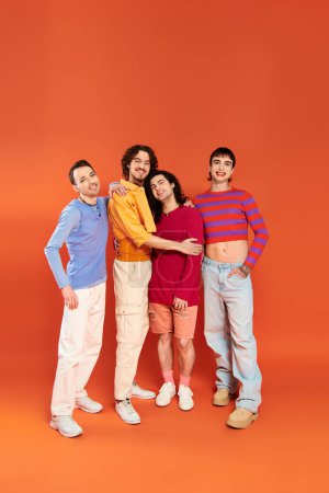 Téléchargez les photos : Quatre beaux hommes gays gais dans des vêtements vibrants posant ensemble sur fond orange, mois de fierté - en image libre de droit