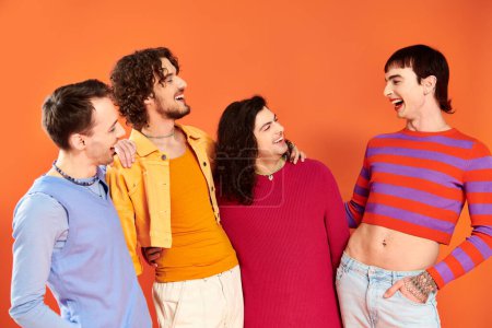 Photo for Four appealing cheerful gay men in vibrant clothes posing together on orange backdrop, pride month - Royalty Free Image