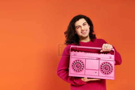 Photo for Merry appealing gay man in magenta sweatshirt with long hair holding tape recorder smiling at camera - Royalty Free Image
