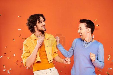 Photo for Positive good looking gay friends in stylish clothes with makeup posing under confetti rain, pride - Royalty Free Image