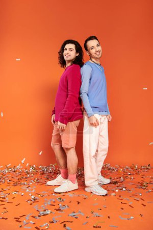 Foto de Alegre bien parecido gay amigos en elegante ropa con maquillaje posando bajo confeti lluvia, orgullo - Imagen libre de derechos