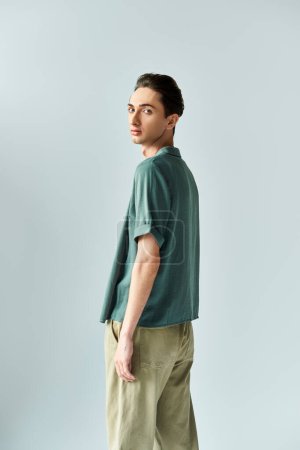 Foto de Joven queer posa orgullosamente en una camisa de polo verde y pantalones caqui sobre un fondo gris del estudio. - Imagen libre de derechos