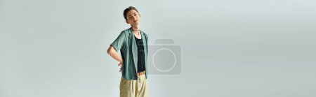 A young queer person confidently poses on a white background in a studio setting.