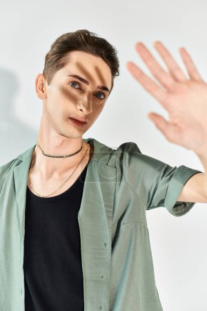 Un joven queer con una camisa verde golpea un gesto de mano, mostrando orgullo e individualidad en un estudio sobre un fondo gris.
