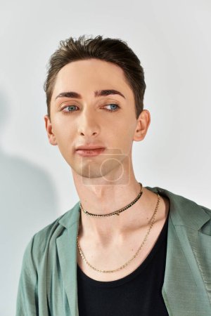 Téléchargez les photos : Une jeune queer pose avec confiance dans une veste verte élégante et un collier frappant sur un fond de studio gris. - en image libre de droit