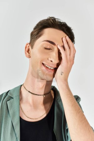 Photo for A young queer person smiling brightly, hands on his face, exuding pride and confidence on a grey studio background. - Royalty Free Image