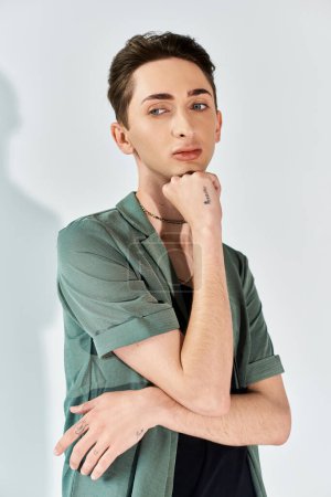 A young man in a green shirt strikes a pensive pose, hand resting on chin, exuding style and confidence in a studio setting.