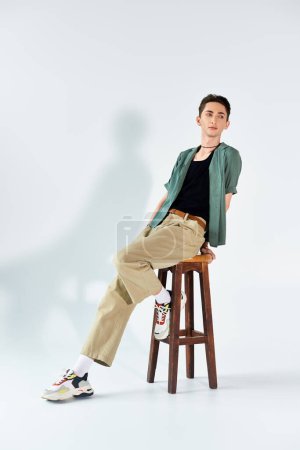 Foto de A young queer person in a thoughtful pose while sitting on a stool against a white backdrop. - Imagen libre de derechos
