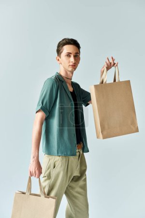 Ein junger queerer Mensch hält fröhlich Einkaufstüten vor leuchtend blauem Hintergrund.