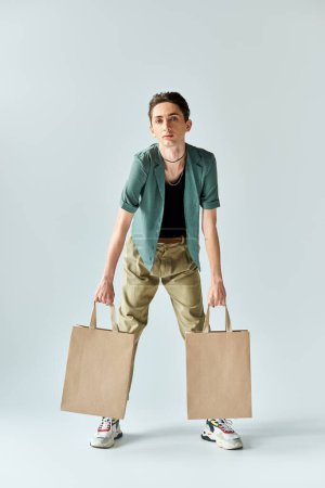 A young queer person holding two shopping bags against a gray background, expressing joy and pride in their purchases.