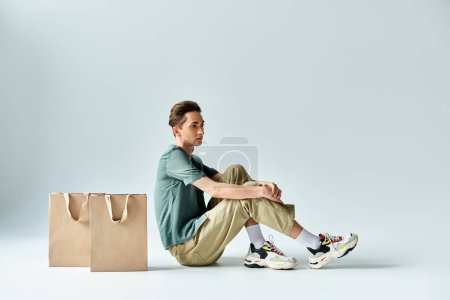 A man, embracing retail therapy, sits on the ground surrounded by shopping bags.