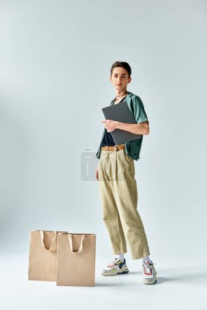 Un joven hace malabares con confianza con las bolsas de la compra y una tableta, mostrando su lado de moda y con conocimientos tecnológicos.