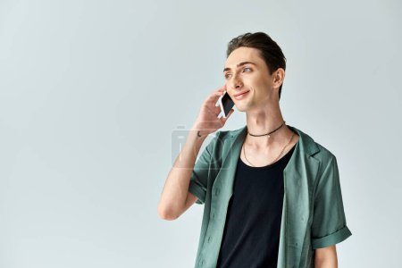 A young queer person deeply engrossed in a phone call against a serene gray background.
