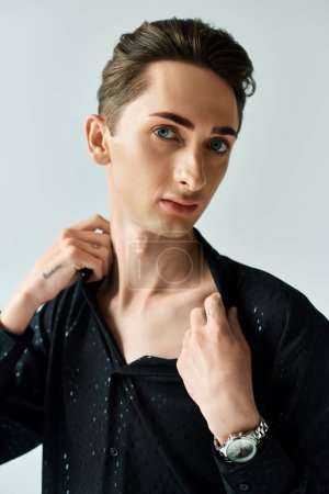 Foto de Un joven con una camisa negra ajusta su cuello, exudando confianza y estilo, en un ambiente de estudio sobre un fondo gris. - Imagen libre de derechos