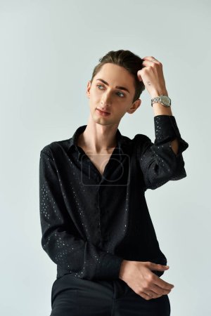 A young man, proudly representing the LGBTQ+ community, poses confidently in a studio against a grey background.