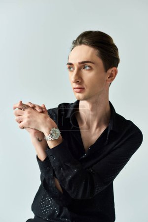 Photo for A young man in a black shirt confidently displays his queer pride as he strikes a pose in a studio against a grey background. - Royalty Free Image