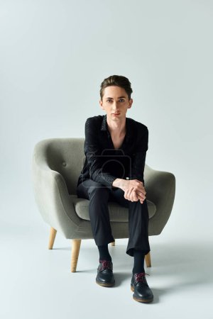 Ein junger queerer Mensch sitzt selbstbewusst auf einem grauen Stuhl im Studio und strahlt Stolz und Selbstbewusstsein aus..