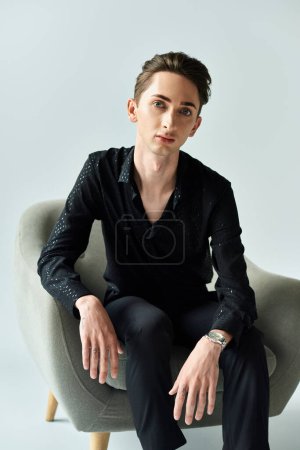 Young queer person exudes confidence, sitting on a chair in a black shirt, portraying strength and individuality.