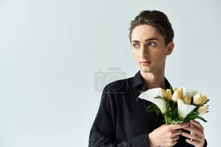 A young queer person holds a vibrant bouquet of flowers in a studio against a grey background.