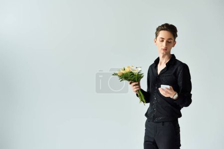 A young queer person holding a bouquet of flowers in a studio setting on a grey background.