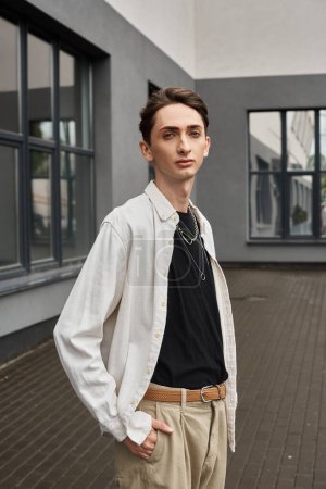 Foto de Un joven queer emana confianza en su camisa blanca y pantalones bronceados, abrazando su estilo único con un toque de orgullo LGBTQ. - Imagen libre de derechos