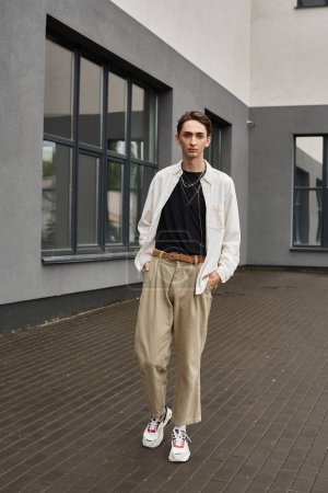 Ein junger queerer Mensch steht selbstbewusst in stylischer Kleidung vor einem Gebäude und strahlt Stolz und Zuversicht aus.