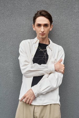 Photo for A young queer person in stylish attire, leaning against a wall in a white shirt, exuding confidence and pride. - Royalty Free Image