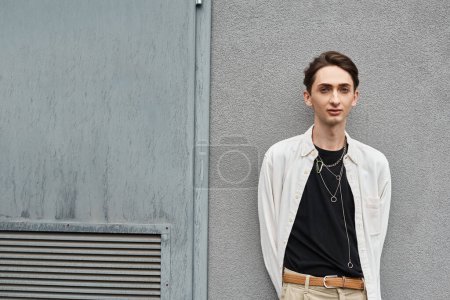 Un joven de moda, miembro de la comunidad LGBT, se apoya contra una pared en un momento de soledad reflexiva.