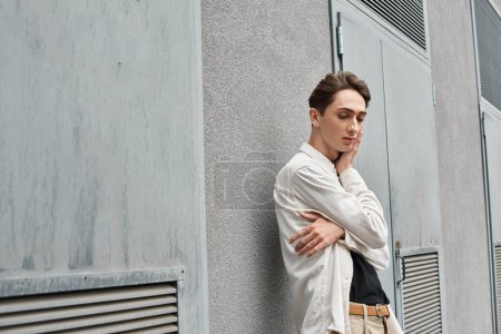 Ein stilvoll gekleideter junger Mensch lehnt an einer Wand verloren in seinen Gedanken und strahlt ein starkes Gefühl der Kontemplation aus.