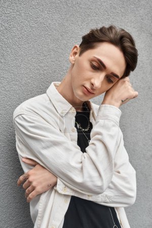 A young man in stylish attire leans against a wall, exuding a sense of rebellion and contemplation.