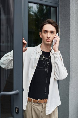 Ein junger Mann, stilvoll gekleidet, plaudert mit einem Handy vor der Tür.