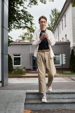 Photo for A young queer person in stylish tan jacket and khaki pants is standing on the steps, exuding confidence and pride. - Royalty Free Image