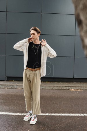 A young queer person in a stylish tan shirt and pants standing confidently on a city street.