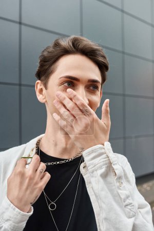 A young individual, part of the LGBTQ community, covers his face with his hands in a gesture of concealment.