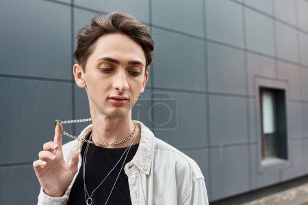 Foto de Un joven y elegante individuo sostiene un collar frente a un majestuoso edificio, mostrando su sentido único de la moda y el orgullo. - Imagen libre de derechos