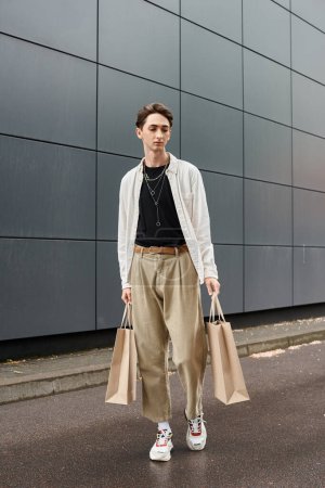 Un joven queer con un atuendo elegante caminando con bolsas de compras frente a un edificio en la ciudad.
