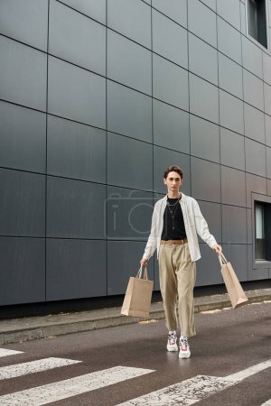 A stylish young queer person walks carrying shopping bags in front of a sleek city building, showcasing confidence and pride.