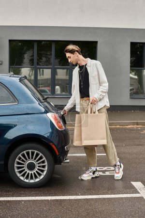 Téléchargez les photos : Un jeune homme queer en tenue élégante se tient à côté d'une voiture de luxe tenant des sacs à provisions. - en image libre de droit
