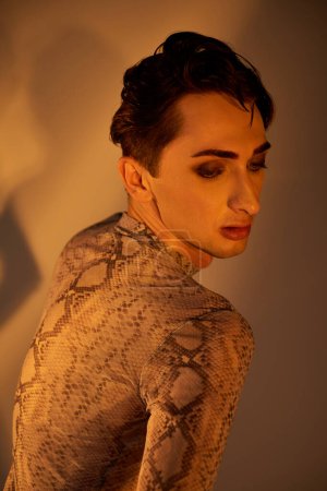 A young queer person poses in front of a mirror wearing a python skin dress, exuding confidence and style.